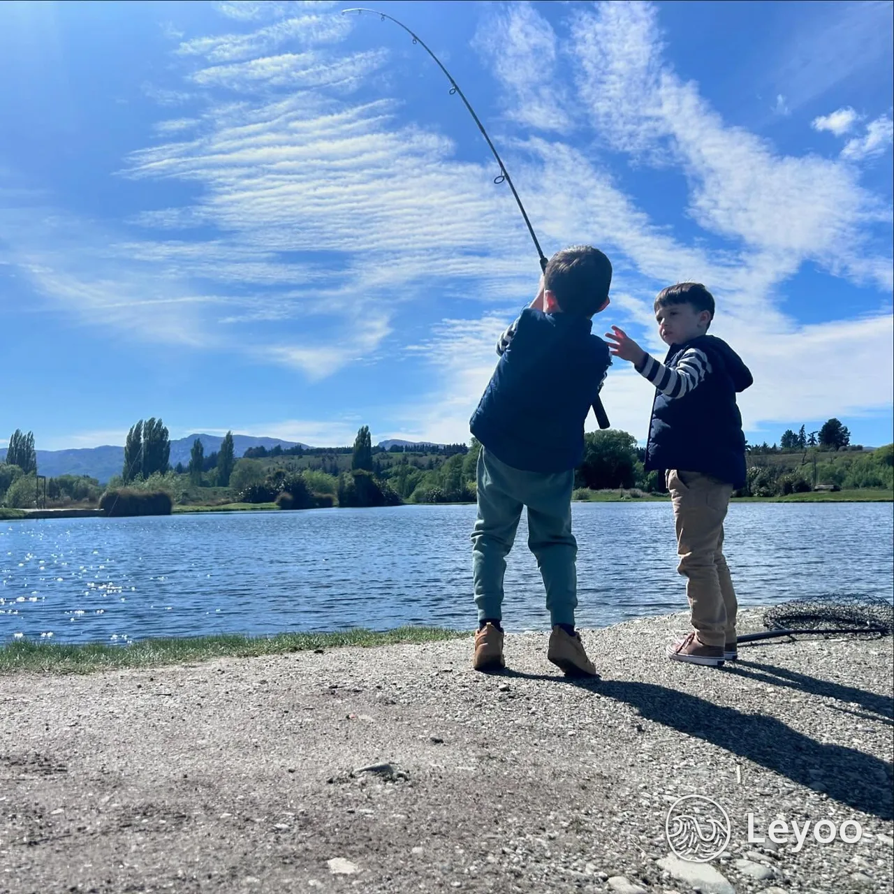 Two children fishing beside a lake in Wanaka, with water and distant hills behind them